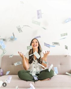 a woman sitting on top of a couch surrounded by money flying in the air above her