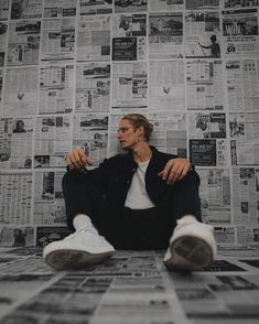 a man sitting on the floor in front of a wall with newspapers all over it