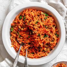 a white bowl filled with carrot salad next to two spoons