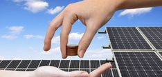 two hands reaching for a stack of coins in front of a solar panel with blue sky and clouds