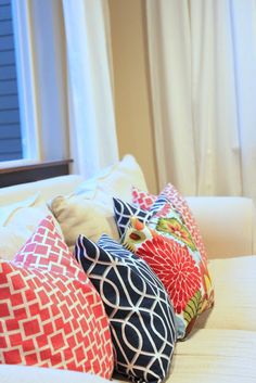 four colorful pillows sitting on top of a white couch in front of a windowsill