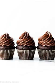 three cupcakes with chocolate frosting on them are lined up in a row