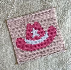 a crocheted pink and white hat hanging from a string on top of a bed