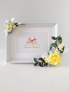 a white frame with yellow and white flowers on it next to a small flower arrangement