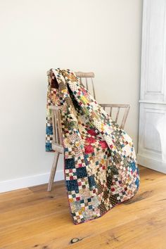 a chair with a quilt on it in front of a white wall and wooden floor