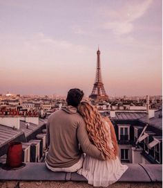 a man and woman sitting on top of a roof looking at the eiffel tower