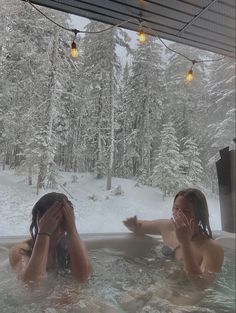 two people in a hot tub with snow on the ground and lights hanging from the ceiling