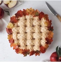 an apple pie with braiding on top surrounded by autumn leaves, apples and a knife