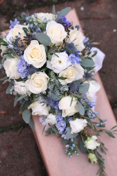 a bridal bouquet sitting on top of a piece of wood with blue and white flowers