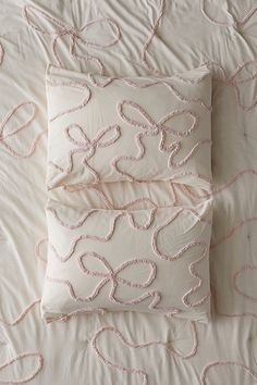 two pillows on top of a bed with white sheets and pink threadwork in the shape of hearts