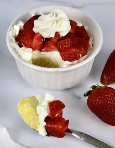 a bowl filled with cake and strawberries on top of a white counter next to a spoon