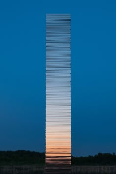 a tall building with many lines on it's side in the night sky, against a background of trees and blue sky