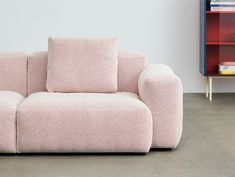 a pink couch sitting on top of a cement floor next to a book shelf filled with books