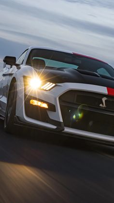 the front end of a white sports car driving on a road at night with bright lights