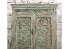 an old wooden cabinet with ornate carvings on the front and side doors, against a stone wall