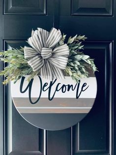 a welcome sign hanging on the front door with a bow and greenery in it