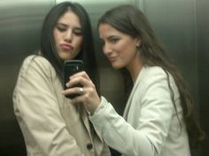 two women looking at their cell phones in an elevator stall, one with her hand on the other's shoulder