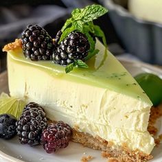 a piece of cheesecake with berries and mint on top sits on a white plate