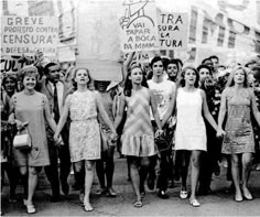 a group of women standing next to each other in front of a crowd holding signs