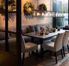 a dining room table and chairs with candles on them in front of a wall decorated with wreaths