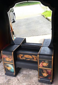 a black vanity with an ornate painted design on the top and bottom drawers is shown in front of a parked car