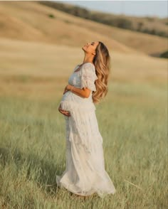 a pregnant woman standing in a field with her hands on her belly and looking up at the sky