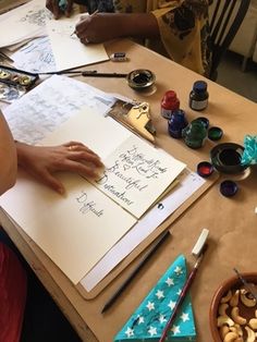 two people sitting at a table working on some art work with markers and paintbrushes