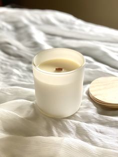 a white candle sitting on top of a bed next to a wooden coaster