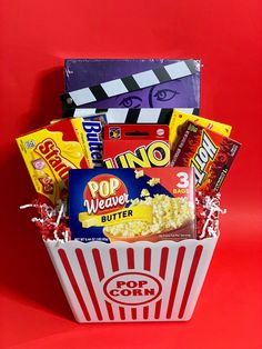 a popcorn bucket filled with snacks and candy on top of a red table next to a movie clapper