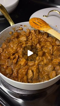 a pan filled with food sitting on top of a stove next to a wooden spoon