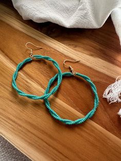 two pairs of turquoise beaded hoop earrings sitting on top of a wooden table next to a white towel