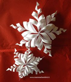 two paper snowflakes sitting on top of a red cloth