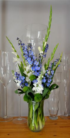 a vase filled with blue and white flowers on top of a wooden table next to wine glasses