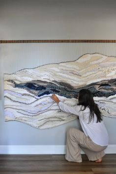 a woman kneeling down in front of a large piece of art that is hanging on the wall