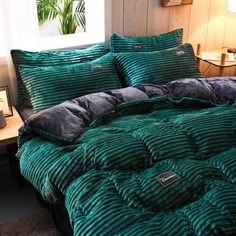 a bed with green comforter and pillows in a room next to a lamp on a table