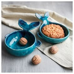 two blue bowls filled with cookies on top of a white cloth next to walnuts