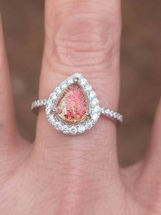 a close up of a person's hand wearing a ring with a pink stone in the middle