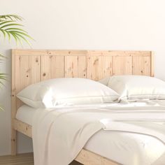 a bed with white sheets and pillows in a room next to a potted plant