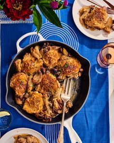 a pan filled with chicken and mushrooms on top of a blue table cloth next to two plates