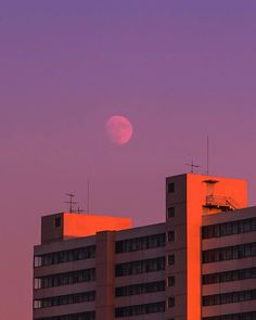 the moon is setting over some buildings in front of a purple sky with no clouds