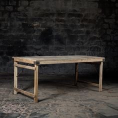 an old wooden table sitting in front of a brick wall with no one around it