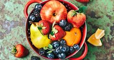 a red bowl filled with assorted fruit on top of a table