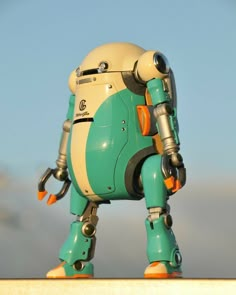 a green and white robot standing on top of a wall next to a blue sky