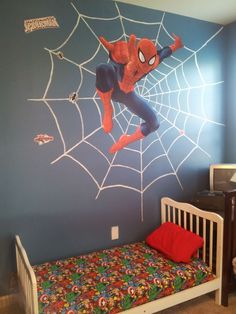 a bedroom with a spiderman mural on the wall next to a toddler's bed