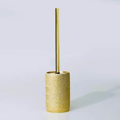 a gold toilet brush holder on a white surface with a long golden rod in the middle