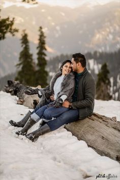 a man and woman are sitting on a log in the snow