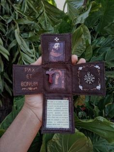 a person holding up a small cross with pictures on it in front of some plants