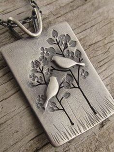 two birds sitting on top of a tree in a metal square pendant hanging from a chain