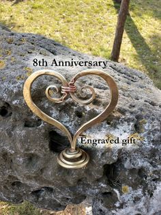 a heart shaped metal object sitting on top of a rock with the words 8th anniversary engraved in it