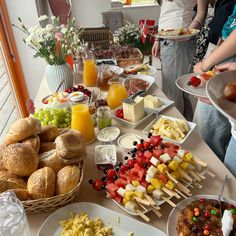 a table full of food and drinks with people standing around the table in the background